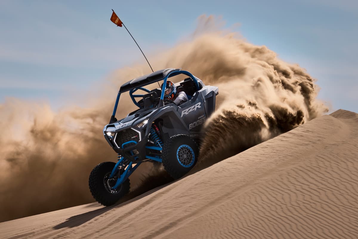 Côte-à-côte Polaris RZR Pro R Boost 2027 gravissant une dune de sable dans un nuage de poussière, nouveauté présentée sur Infoquad.ca