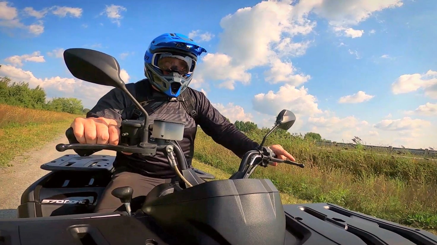 Blue-helmeted rider driving a Snarler AT6 ATV on a dirt road in sunny weather.