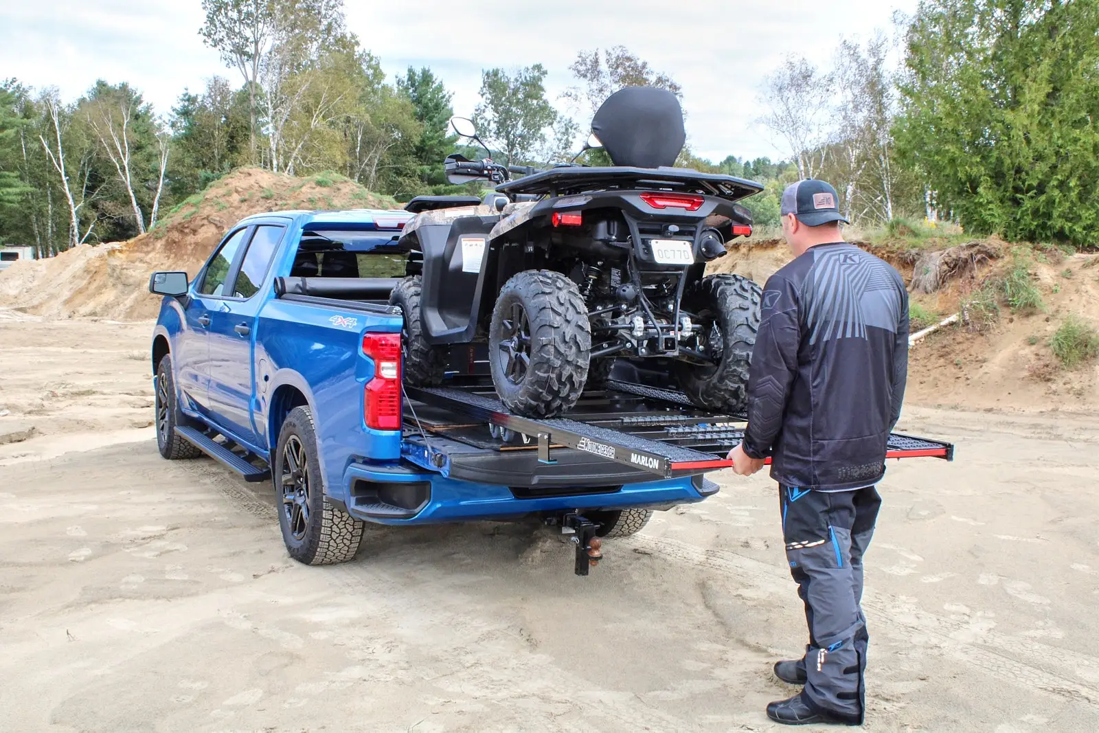 A man loading a Segway ATV into a blue pickup bed using a Single Loader ramp on sandy terrain.