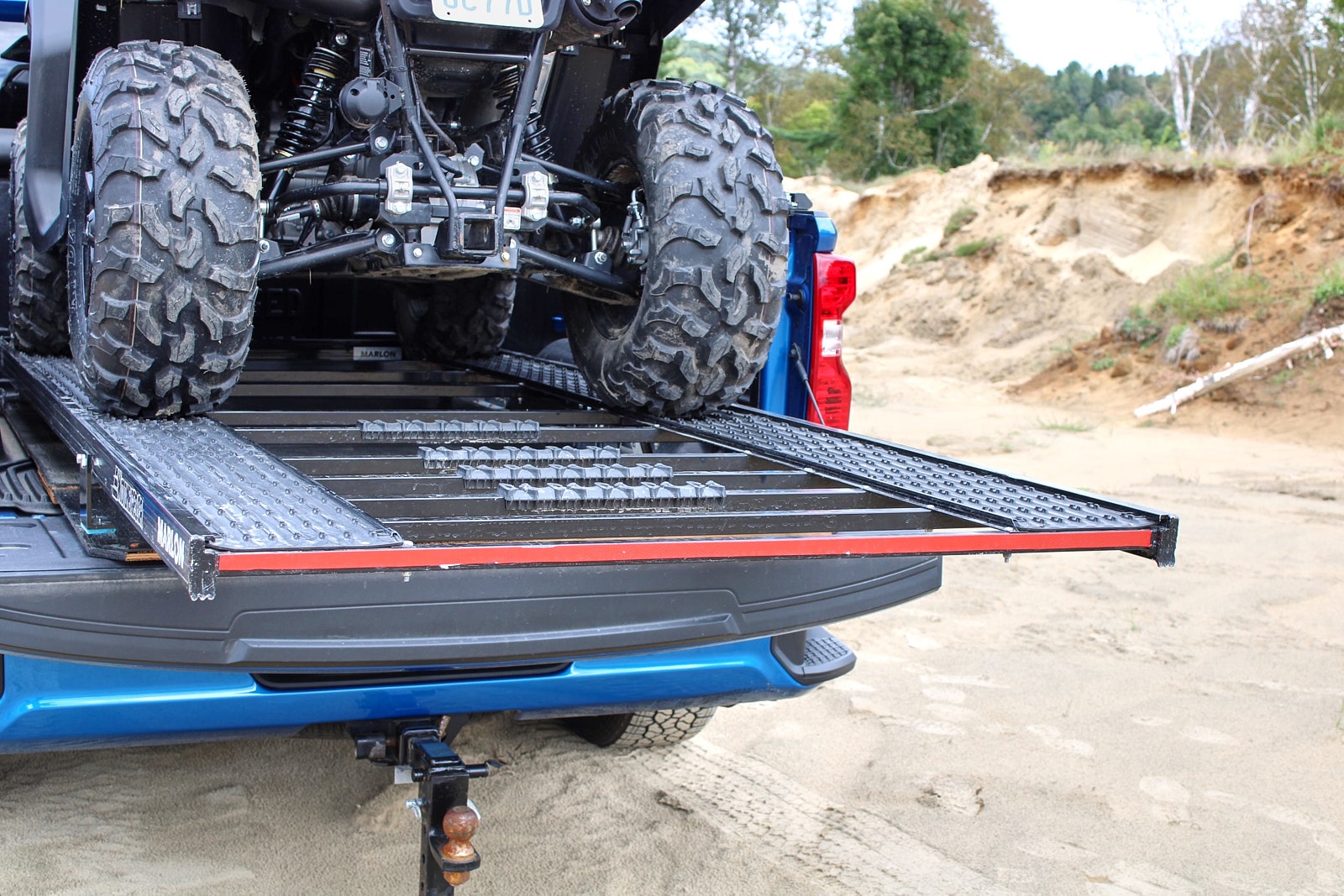 Gros plan des roues arrière d’un VTT Segway sur une rampe de chargement installée sur le plateau d’un pick-up bleu.