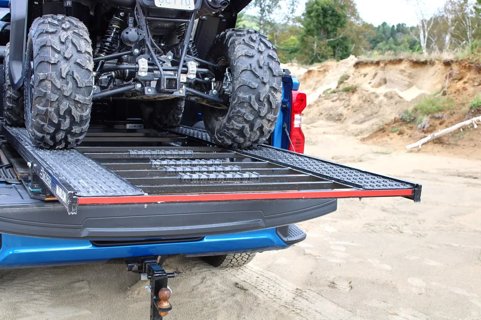 Close-up of the rear wheels of a Segway ATV on a loading ramp installed on the bed of a blue pickup truck.