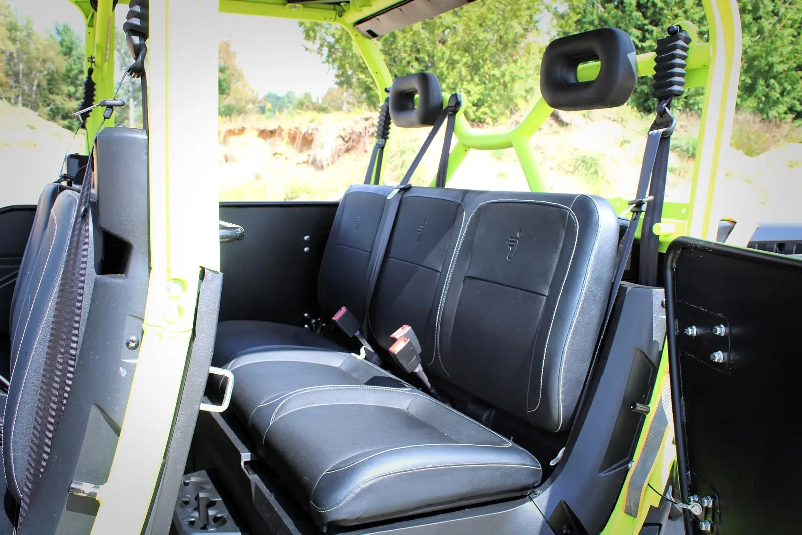 Interior view of a Segway Fugleman UT10 Crew, showing black rear seats with contrasting stitching, seatbelts, and a bright yellow protective tube frame.