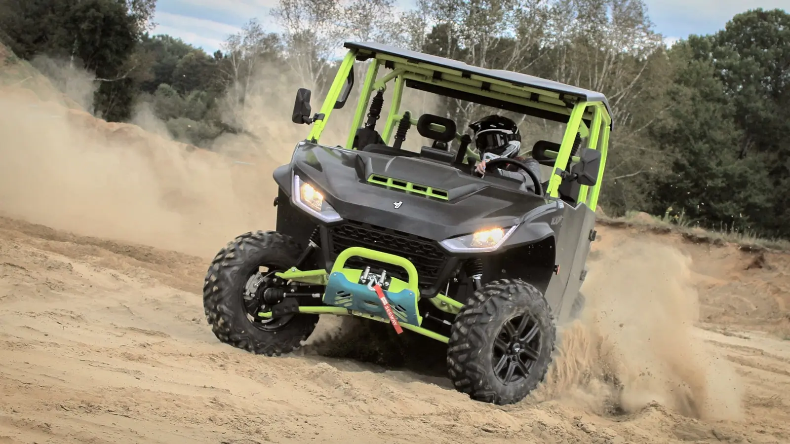 A Fugleman UT10 Crew utility side-by-side kicking up a cloud of dust on sandy terrain, with the driver wearing a helmet and the vehicle equipped with a front guard and winch.