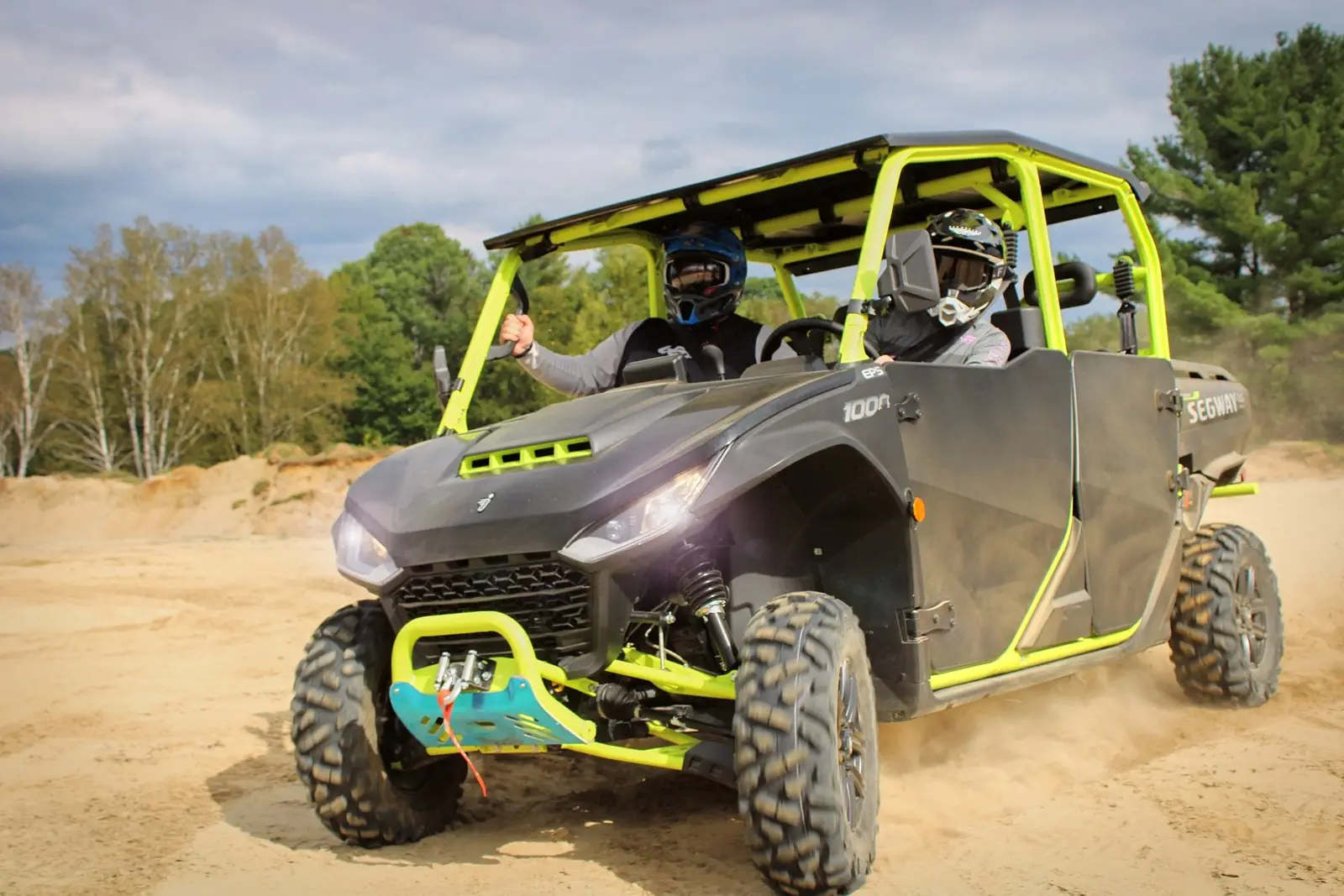 Two people riding a Segway Fugleman UT10 Crew on sandy terrain, with the passenger giving a thumbs-up in satisfaction.